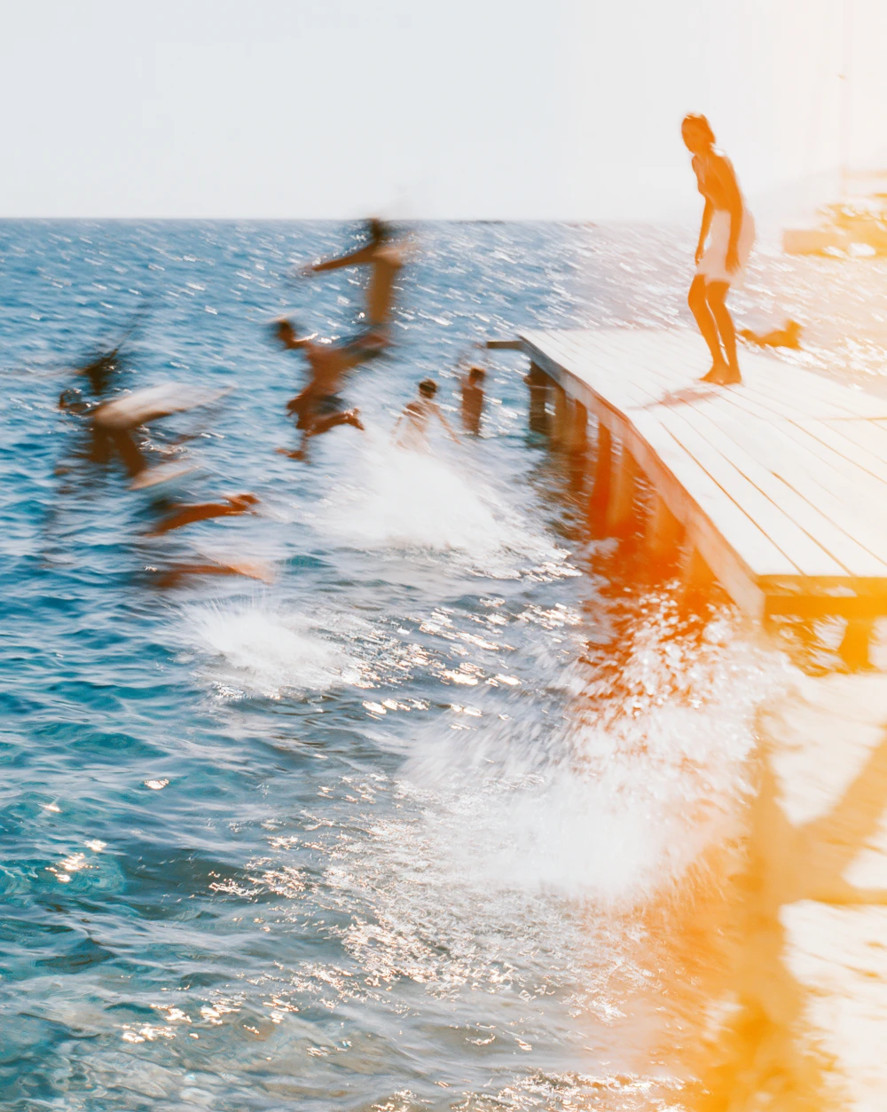 Summer scene, figures jumping from a jetty into the sea